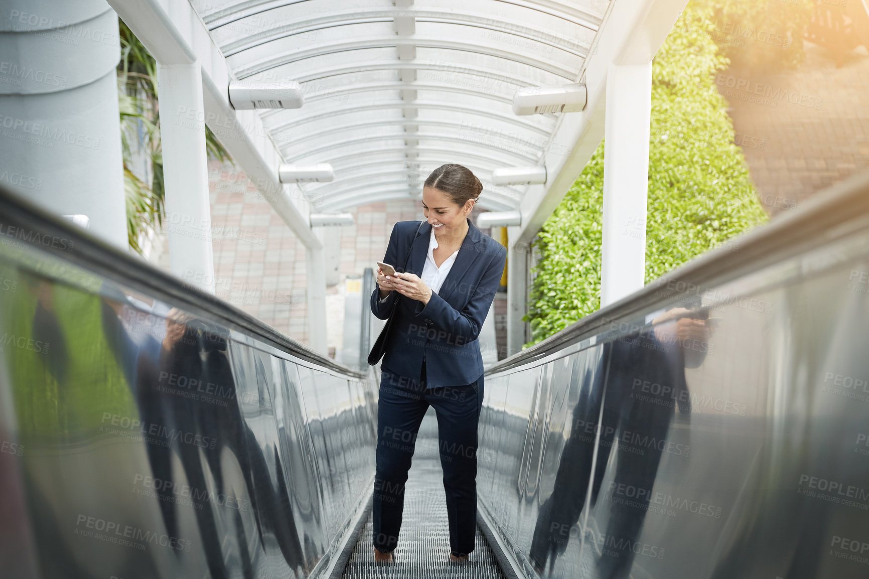 Buy stock photo Shot of a young businesswoman using a cellphone on an escalator