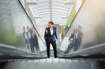 Buy stock photo Shot of a young businesswoman using a cellphone on an escalator