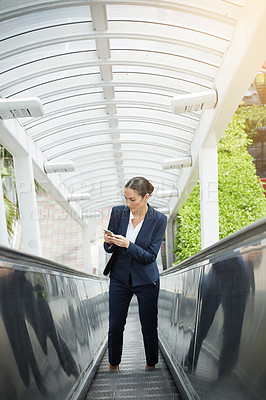 Buy stock photo Shot of a young businesswoman using a cellphone on an escalator