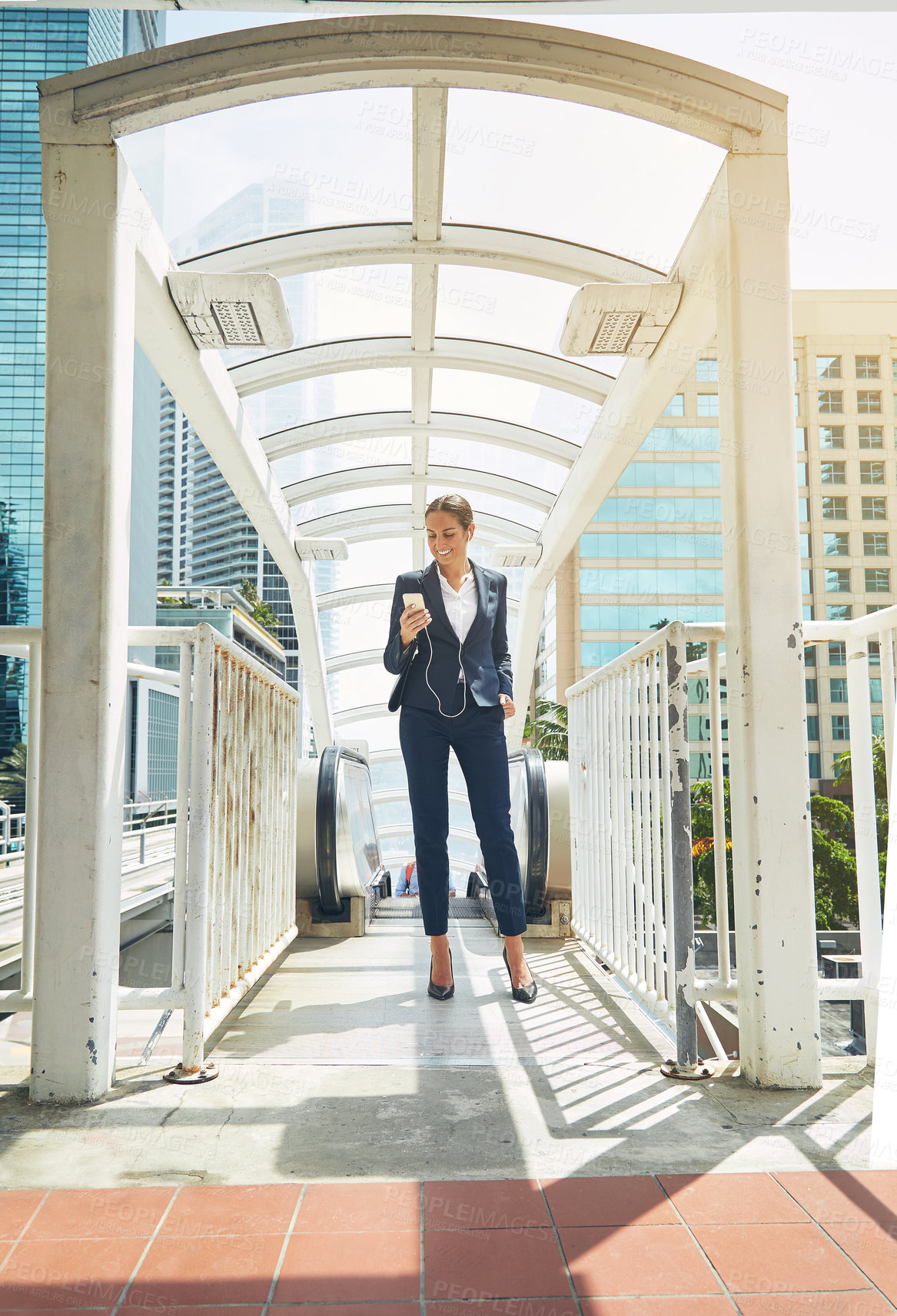 Buy stock photo Shot of a young businesswoman using a cellphone while getting off an escalator