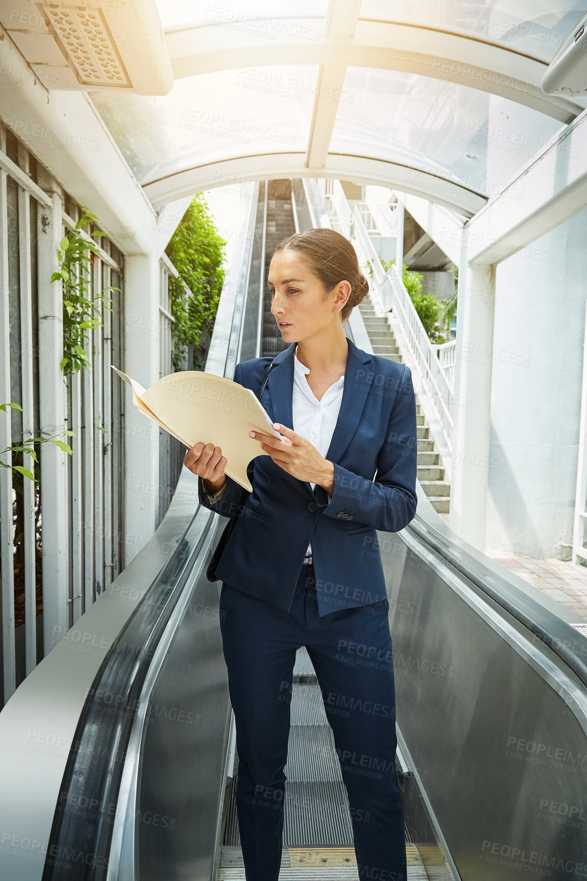 Buy stock photo Shot of a young businesswoman reading paperwork on an escalator