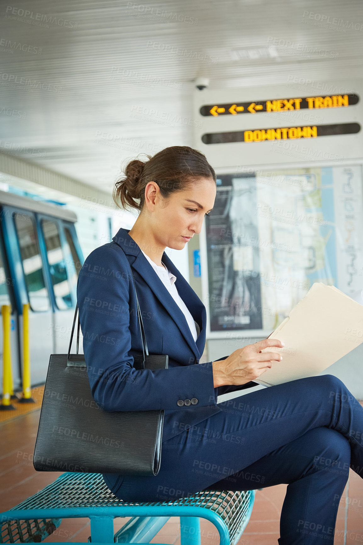 Buy stock photo Shot of a businesswoman reading paperwork while waiting at a public transport stop