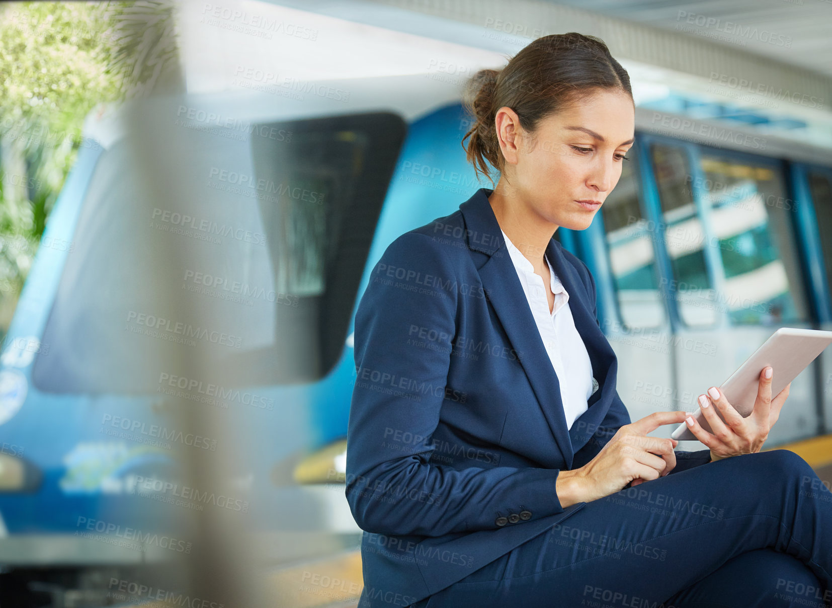 Buy stock photo Shot of a businesswoman using a digital tablet while waiting at a public transport stop