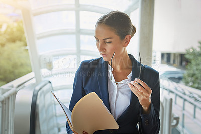 Buy stock photo Shot of a young businesswoman reading paperwork on her way to the office