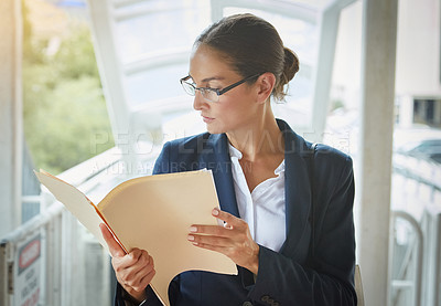 Buy stock photo Shot of a young businesswoman reading paperwork on her way to the office