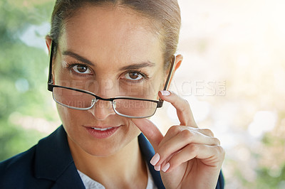 Buy stock photo Portrait of a young businesswoman peering over the rim of her glasses while standing outside