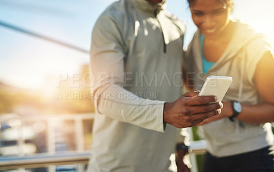 Buy stock photo Shot of a young sporty couple using a cellphone outside