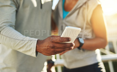 Buy stock photo Shot of a young sporty couple using a cellphone outside