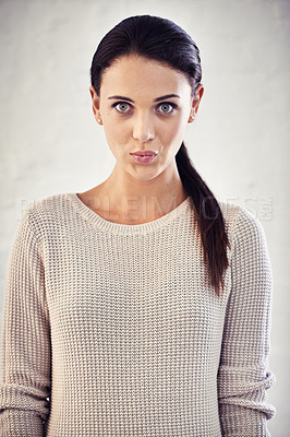 Buy stock photo Portrait of a serious looking young woman standing against a brick wall