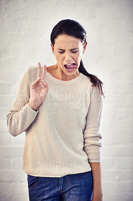Buy stock photo Shot of a young woman sticking out her tongue while making the peace sign