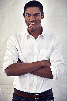 Buy stock photo Portrait of a young man with his arms crossed sticking out his tongue
