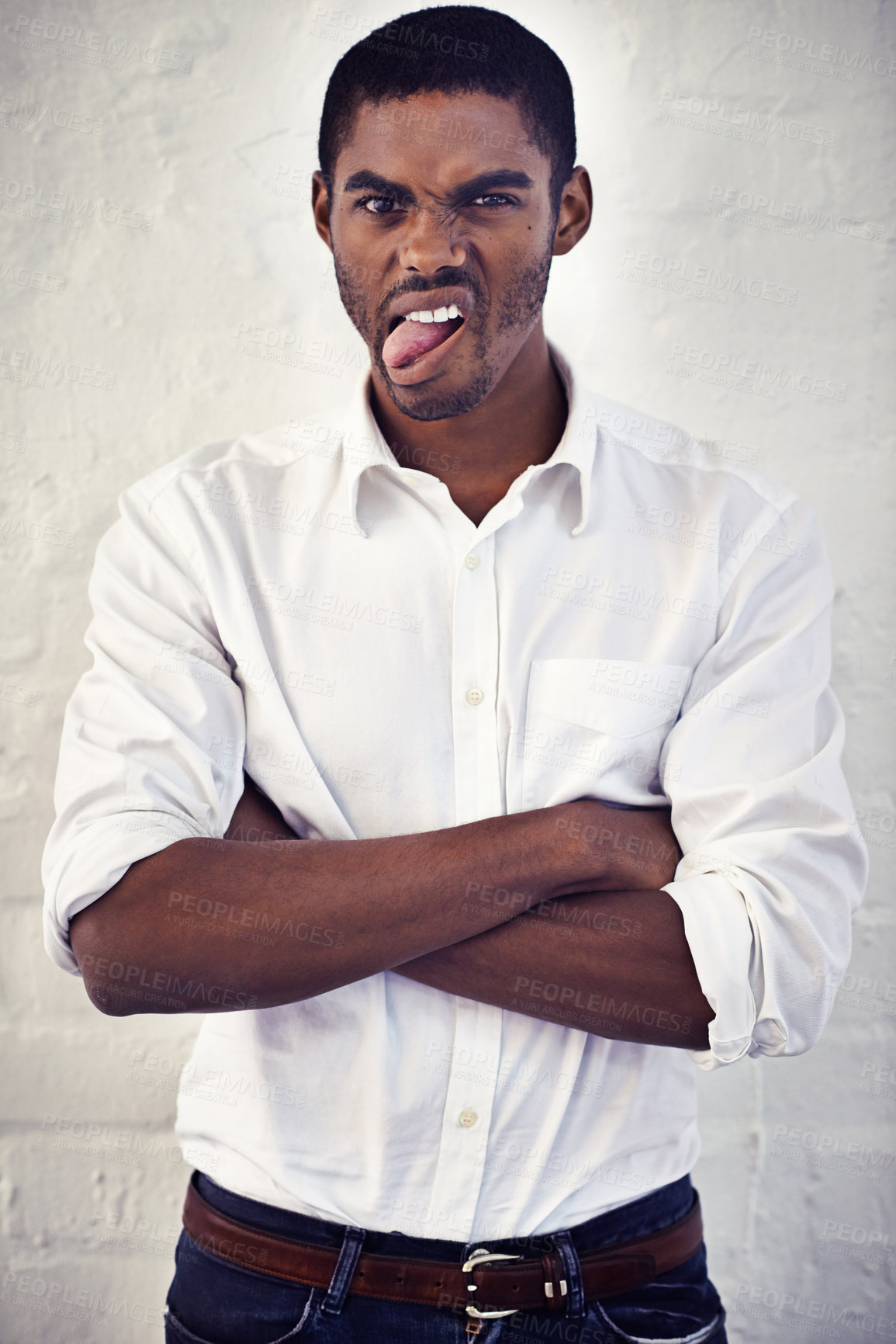 Buy stock photo Portrait of a young man with his arms crossed sticking out his tongue