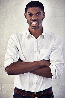 Buy stock photo Shot of a serious young man standing with his arms crossed