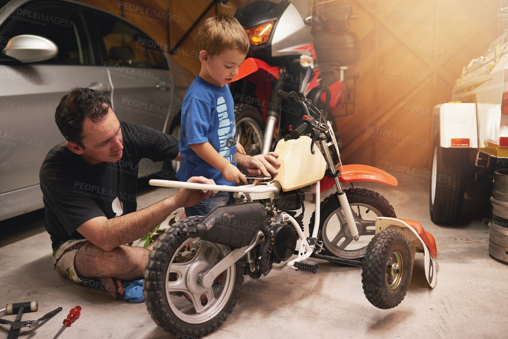 Buy stock photo Family, child and fixing with bike in garage at home for teamwork, support and repair with tools. Parent, father and son for bonding, helping and together as mechanic for motorbike in carport