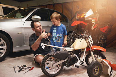 Buy stock photo Shot of a father and son fixing a bike in a garage