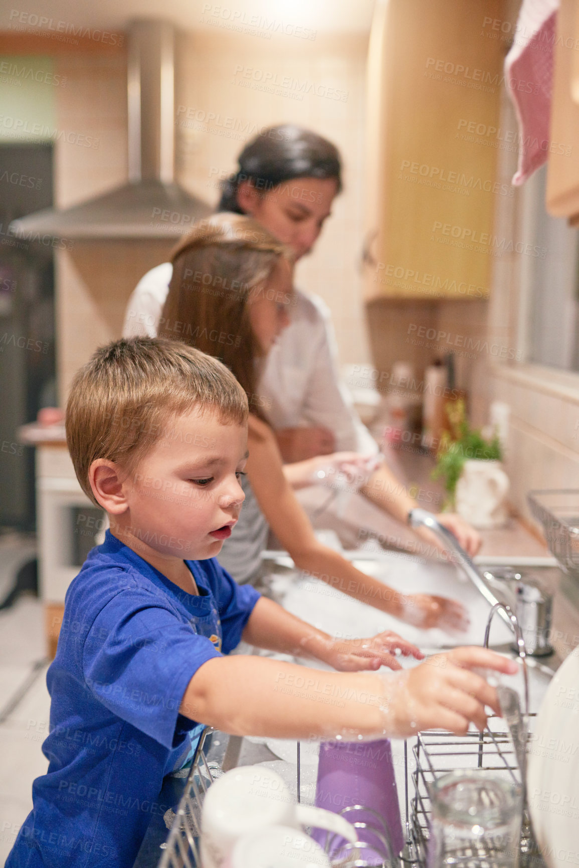 Buy stock photo Shot of a little boy washing dishes with his family at a kitchen sink