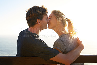 Buy stock photo Shot of a loving couple sitting on a bench overlooking the ocean