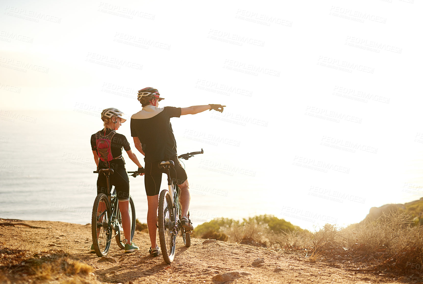 Buy stock photo Shot of a young couple admiring the view from a hilltop while out on a bike ride