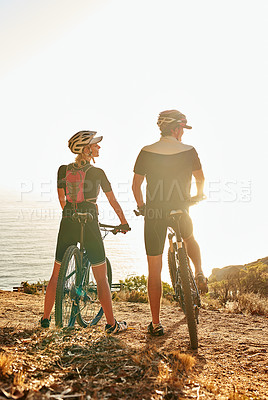 Buy stock photo Shot of a young couple admiring the view from a hilltop while out on a bike ride
