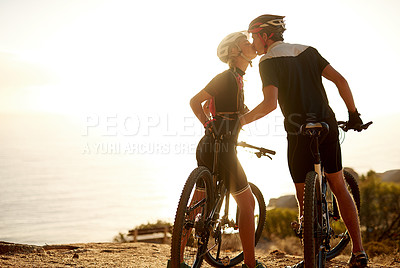 Buy stock photo Shot of a young couple kissing on a hilltop while out on a bike ride