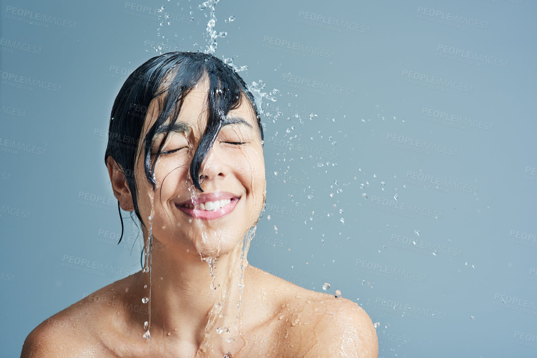 Buy stock photo Shower, beauty and face of woman with water in studio on blue background for wellness, cleaning and grooming. Skincare, bathroom and female person with splash for washing hair, body and cleansing