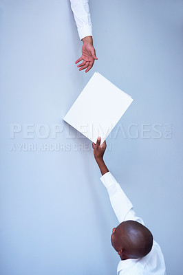Buy stock photo Shot of a young businessman reaching up to pass a file to his unidentifiable colleague