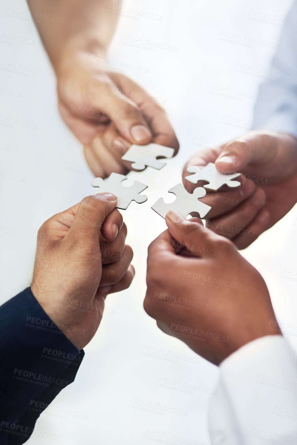 Buy stock photo High angle shot of a group of unidentifiable businesspeople holding puzzle pieces together