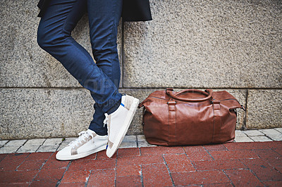 Buy stock photo Cropped shot of a man wearing jeans and sneakers standing next to his bag on a city sidewalk