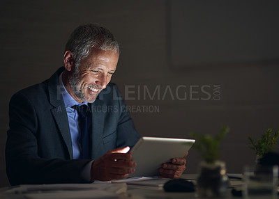 Buy stock photo Shot of a mature businessman using a digital tablet while working late in an office