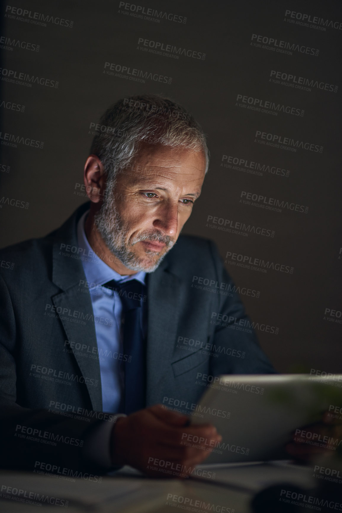 Buy stock photo Shot of a mature businessman using a digital tablet while working late in an office