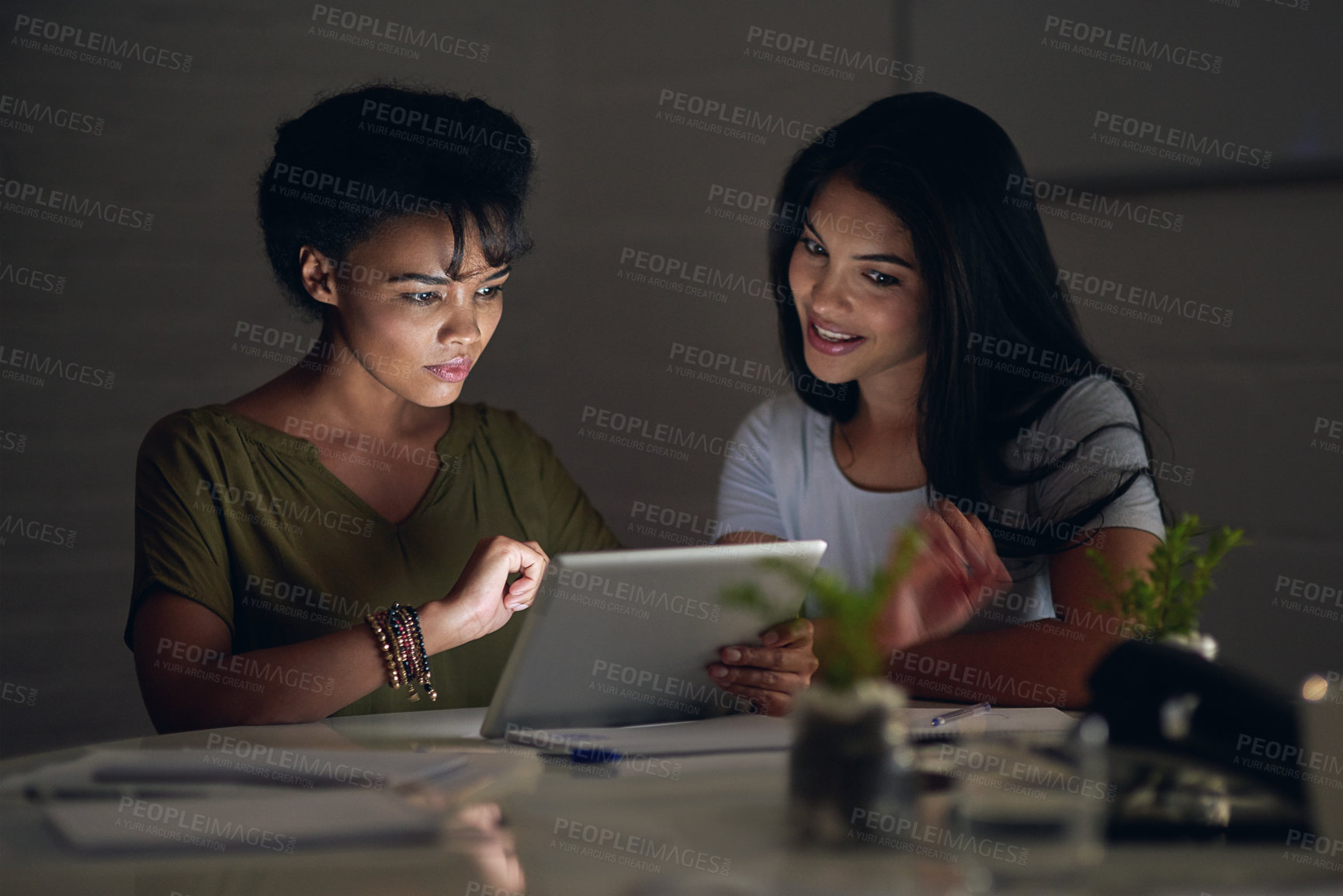 Buy stock photo Shot of two colleagues using a digital tablet while working late in an office