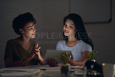 Buy stock photo Shot of two colleagues using a digital tablet while working late in an office