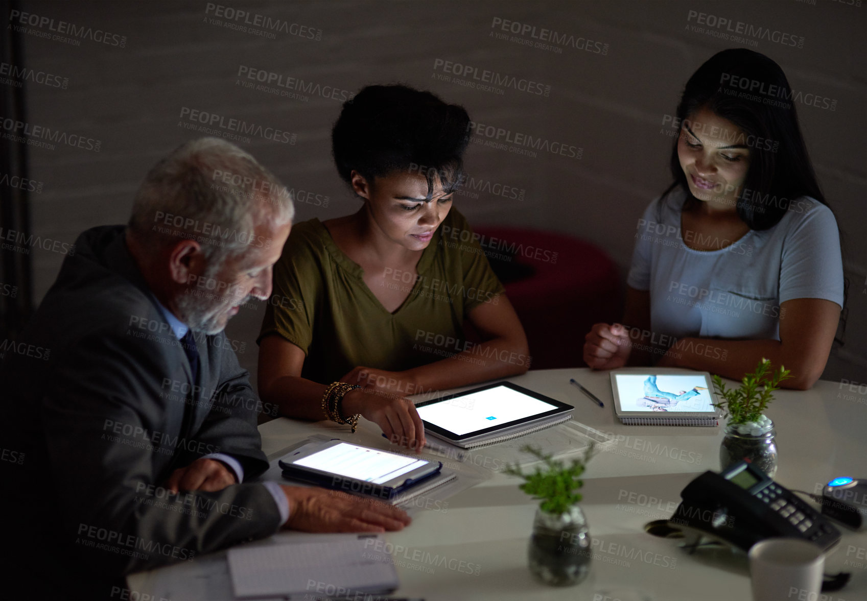 Buy stock photo Shot of a group colleagues using digital tablets while working late in an office