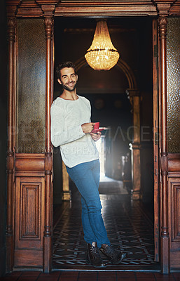 Buy stock photo Portrait of a handsome man standing in the doorway of a cafe holding a cup of coffee