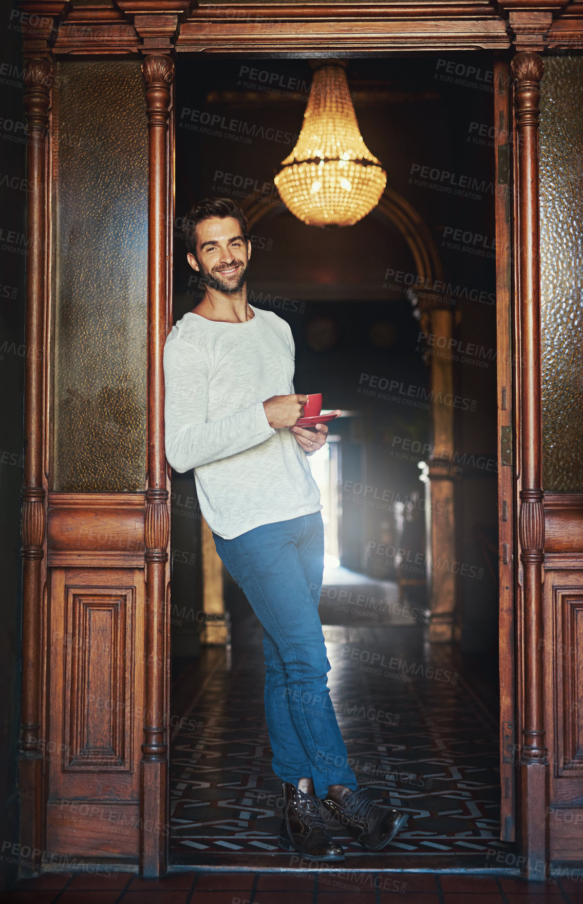 Buy stock photo Portrait of a handsome man standing in the doorway of a cafe holding a cup of coffee
