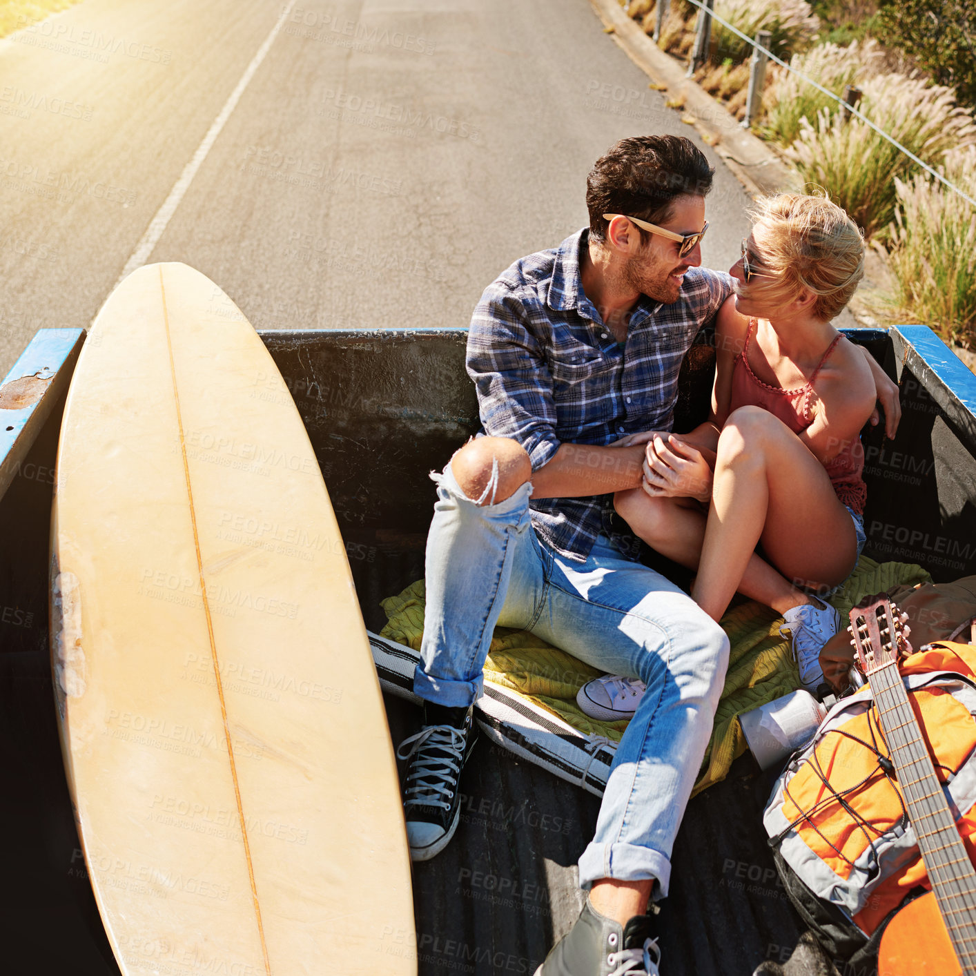 Buy stock photo Shot of a young couple relaxing on the back of a pickup truck while on a road trip