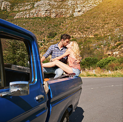 Buy stock photo Shot of a young couple sharing a kiss whole on the back of a pickup truck