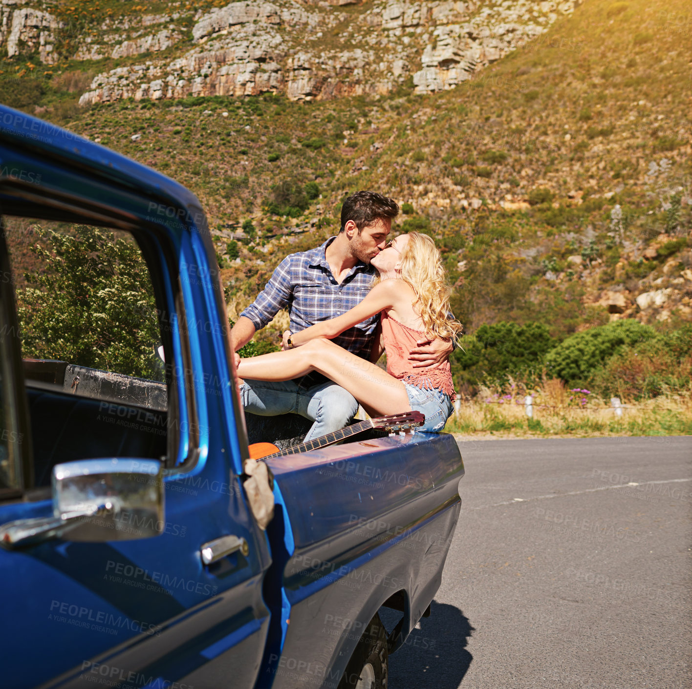 Buy stock photo Shot of a young couple sharing a kiss whole on the back of a pickup truck