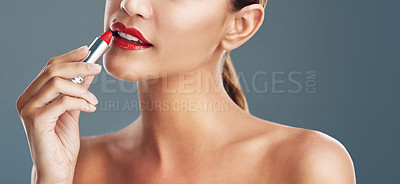 Buy stock photo Studio shot of a beautiful young woman putting on red lipstick against a grey background