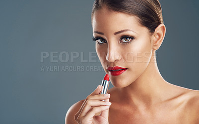 Buy stock photo Studio portrait of a beautiful young woman putting on red lipstick against a grey background