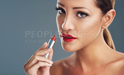 Buy stock photo Studio portrait of a beautiful young woman putting on red lipstick against a grey background