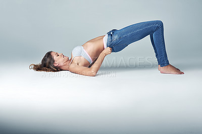 Buy stock photo Studio, fashion and woman with jeans for getting ready, dressing and challenge on grey background. Female person, denim and tight pants with struggle for weight gain, diet and stretching on floor