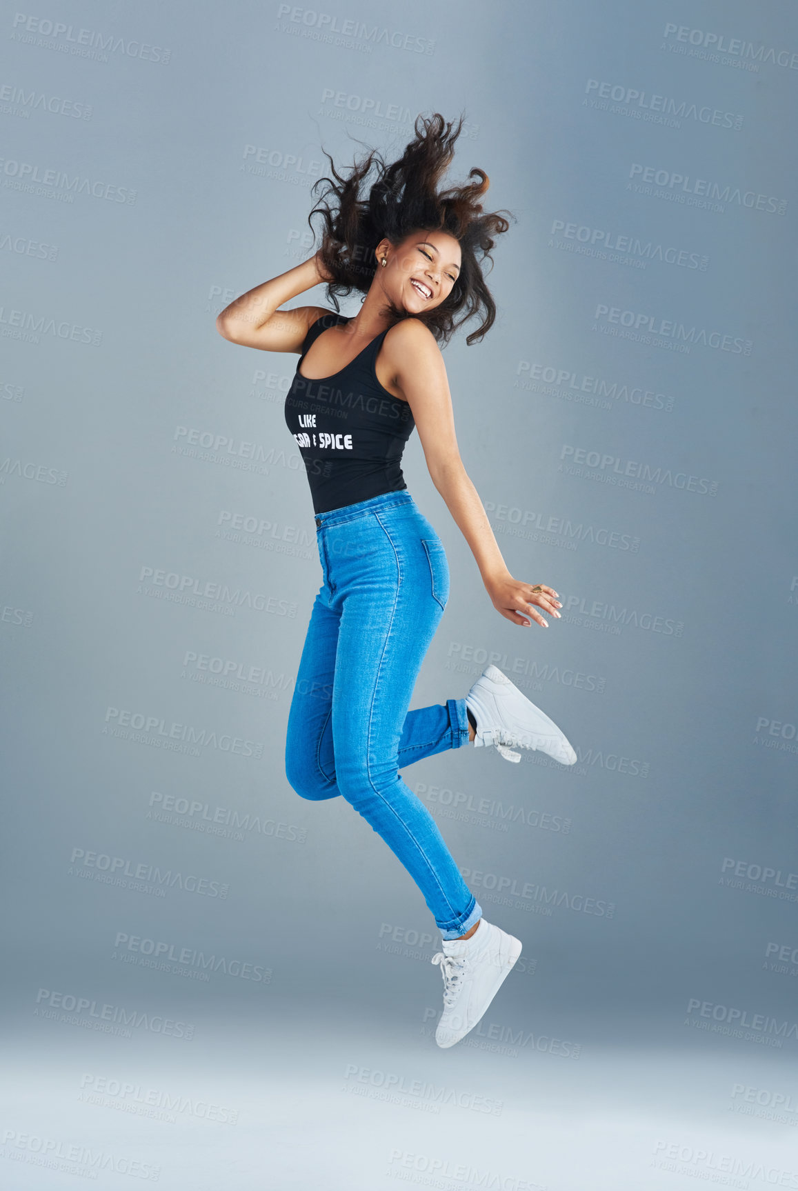 Buy stock photo Happy woman, fun and jump with fashion in air for excitement, style or casual clothing on a gray studio background. Young, female person or excited model with smile in joy for outfit or freedom