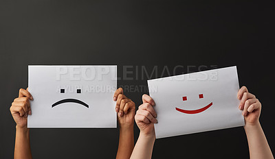 Buy stock photo Shot of two people holding a sign with happy and sad smileys on against a dark background
