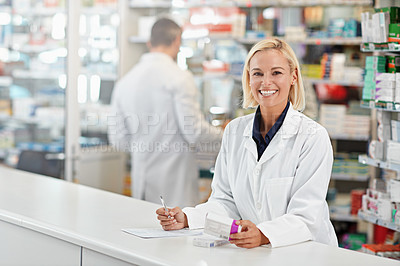 Buy stock photo Shot of a pharmacist at work with her colleague in the background. All products have been altered to be void of copyright infringements