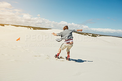 Buy stock photo Rearview shot of a young man sand boarding in the desert