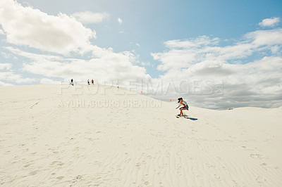 Buy stock photo Shot of a young woman sand boarding in the desert