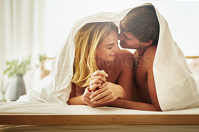 Buy stock photo Shot of a young couple sharing an intimate moment under the covers in bed