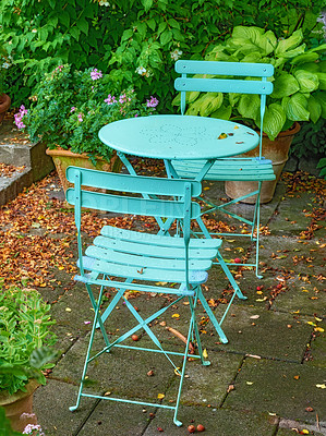 Buy stock photo A calm and relaxing garden with antique table and chairs. Handcrafted metal furniture on a patio or veranda during summer. View of an exterior with green plants and dry leaves scattered on the floor