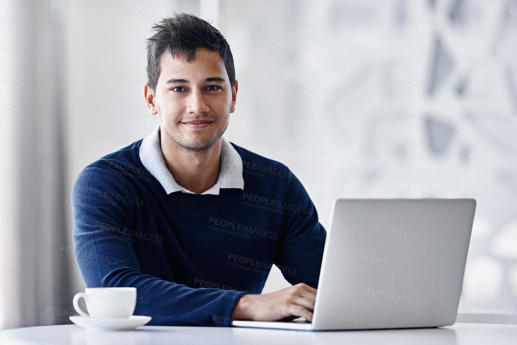 Buy stock photo Portrait of a young businessman using a laptop while sitting at a desk in an office